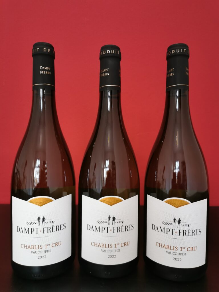 Drei Flaschen DAMPT FRÈRES Chablis 1er Cru Vaucopin 2022 vor rotem Hintergrund