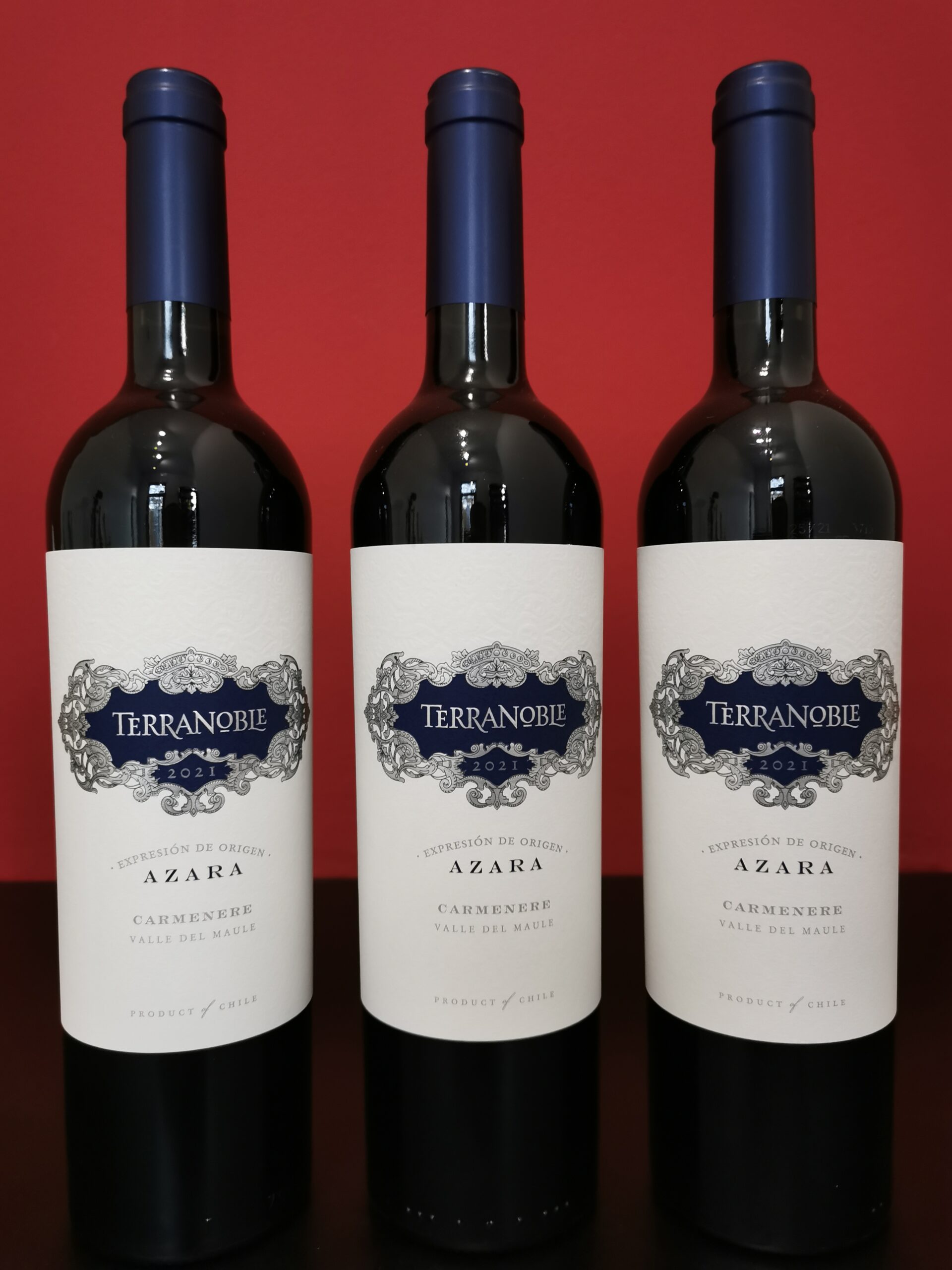 Drei Flaschen TERRANOBLE Azara Carmenere 2021 vor rotem Hintergrund